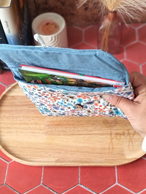 Vue en prise en main d'une livre inséré dans la pochette livre de poche tissu Hortense Bleu montrant sa doublure bleue