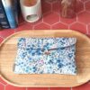 Pochette livre de poche tissu matelassée motif Romane aux fleurs bleues posée sur un plateau en bois