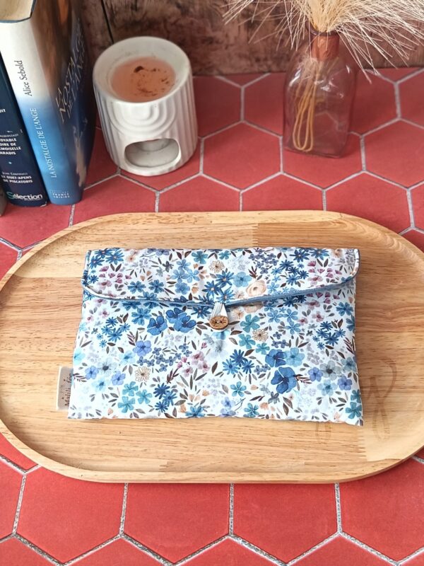 Pochette livre de poche tissu matelassée motif Romane aux fleurs bleues posée sur un plateau en bois